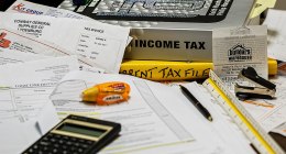 Carpetas y facturas sobre una mesa con una calculadora, un lápiz y una regla, con la carpeta de 'Income tax' en el centro