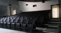 Sala de cine vacía con filas de butacas negras y la pantalla al fondo