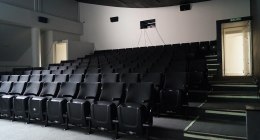 Sala de cine vacía con filas de butacas negras y la pantalla al fondo