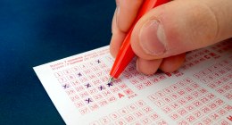 Mano con bolígrafo rojo marcando números en un boleto de lotería