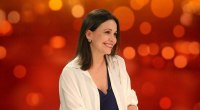 María Corina Machado sonriente, sentada frente a un fondo naranja, en un set de televisión