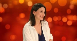 María Corina Machado sonriente, sentada frente a un fondo naranja, en un set de televisión