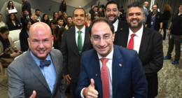 Cinco hombres con traje sonríen en una sala con asistentes detrás; dos hacen pulgar arriba