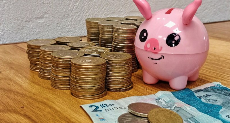 Monedas apiladas, un billete de 2.000 pesos colombianos y una alcancía rosada con forma de cerdito sobre una mesa de madera