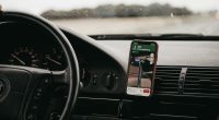 Celular con una app de navegación sujeto en el tablero de un carro, con la carretera al fondo