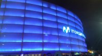 Movistar Arena de Bogotá iluminado de azul de noche, con público a la entrada de un concierto