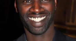 Omar Sy, actor principal de Lupin, sonriendo con traje oscuro en un evento (2012)