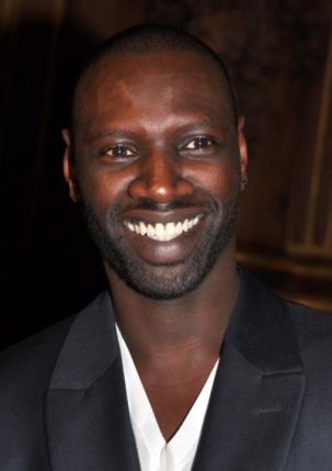 Omar Sy, actor principal de Lupin, sonriendo con traje oscuro en un evento (2012)