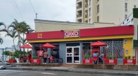 Fachada roja y amarilla de una tienda OXXO en Armenia, Quindío, con mesas en la acera