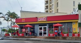 Fachada roja y amarilla de una tienda OXXO en Armenia, Quindío, con mesas en la acera