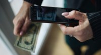 Manos de una persona fotografiando un billete de dólar con su celular, en una escena de pago