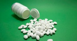 Frasco blanco volcado con pastillas blancas sobre fondo verde