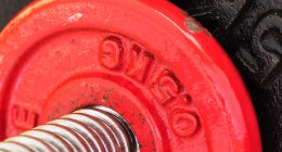 Primer plano de un disco de pesas rojo con la superficie gastada, sobre una barra de acero