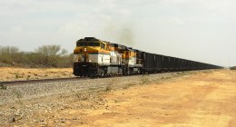 Tren de carbón del Cerrejón, con locomotoras amarillas y blancas y vagones negros, por un camino de tierra en La Guajira