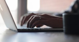 Manos escribiendo en el teclado de un portátil, con la luz de una ventana al fondo
