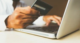 Persona con una tarjeta negra en la mano, frente a un computador portátil, para pagar en línea