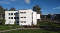 Edificio blanco de la Facultad de Ingeniería de la Universidad Nacional de Colombia, con zonas verdes y estudiantes adultos de paso