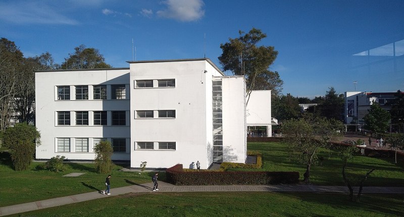 Edificio blanco de la Facultad de Ingeniería de la Universidad Nacional de Colombia, con zonas verdes y estudiantes adultos de paso