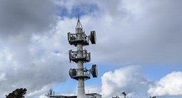 Torre de telecomunicaciones de metal blanco con antenas parabólicas y cielo nublado al fondo