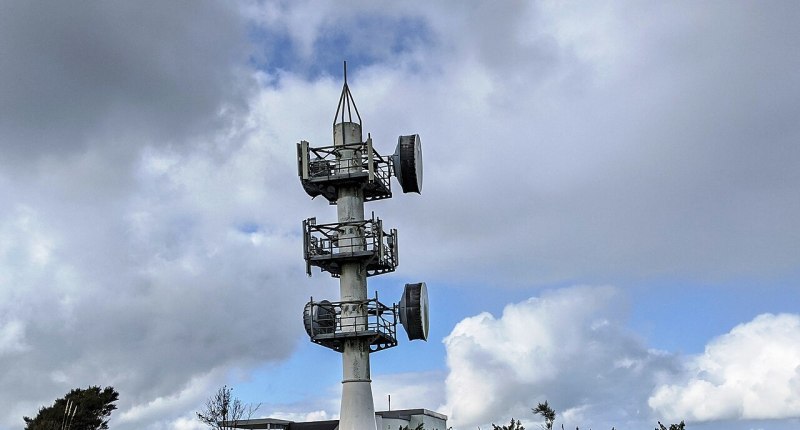 Torre de telecomunicaciones de metal blanco con antenas parabólicas y cielo nublado al fondo